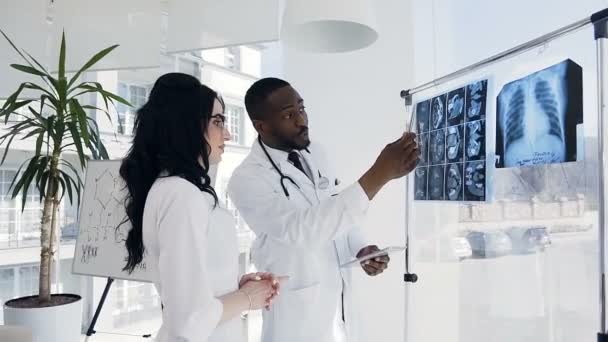 Jovens médicos africanos do sexo masculino e caucasiano do sexo feminino falando sobre impressões de raio-x do paciente . — Vídeo de Stock
