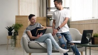 Mutlu gay çift erkekler birlikte kanepede kitap okuyorsun. Okuma kitap onun gay partner sırasında onun ileri oturdu için yaklaştı ve ne okuduğu izler koltukta oturan genç yakışıklı gay adam