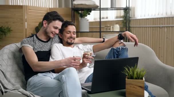 Homoseksueel paar, homoseksuelen, hetzelfde geslacht een huwelijk tussen blanke mannen. Gelukkige homo paar drinken van wijn tijdens het kijken naar films op laptop liggend op de Bank in de woonkamer — Stockvideo