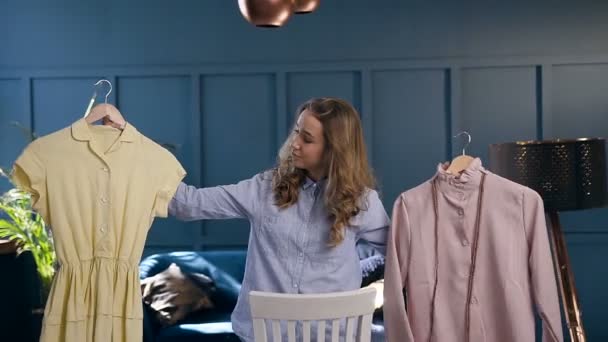 Roztomilá mladá žena s oblečením v rukou při výběru oblečení. — Stock video