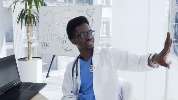 A young afro american doctor with x-ray of female lungs and pelvis is meeting with colleagues and discussing history of the disease patient. Hospital, profession, people and medicine concept — Stock Video