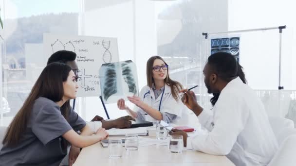 Terapeuta caucásica que habla sobre el trabajo en el hospital a los internos. Están analizando los pulmones de rayos X del paciente del hombre. Hospital, profesión, educación médica, personas y concepto de medicina — Vídeos de Stock