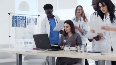 Hastanede tıbbi raporları inceleyerek çok etnik uzman doktorlar ekibi. Hastanedeki çalışma gününde dizüstü bilgisayar ve kağıt belgelerini kullanarak konferans yapan tıp stajyerleri ve doktorlar grubu
