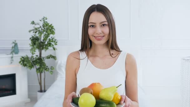 Portrait of attractive caucasian woman stretching out plate with fruits to the camera. — Stock Video