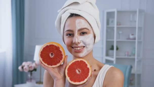 Portret shot van knappe jonge vrouw poseren met twee helft van grapefruit met masker op de helft van het gezicht. — Stockvideo