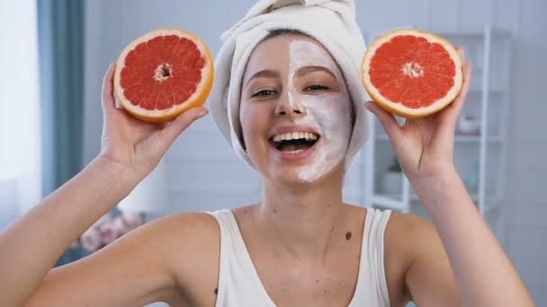 Portret shot van knappe jonge vrouw poseren met twee helft van grapefruit op de ogen met masker op de helft van het gezicht. — Stockvideo