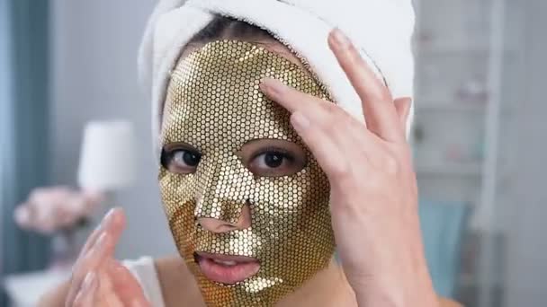 Close-up shot van glimlachende vrouw tot verjonging cosmetische gouden tissue masker op het gezicht. — Stockvideo