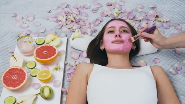 Bovenaanzicht van jonge vrouw ontspannen in Wellness-centrum, terwijl schoonheidsspecialiste toepassing roze masker. — Stockvideo