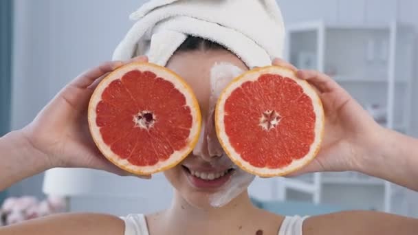 Aantrekkelijke Glimlachende vrouw poseren met twee helft van grapefruit op de ogen met masker op de helft van het gezicht. — Stockvideo