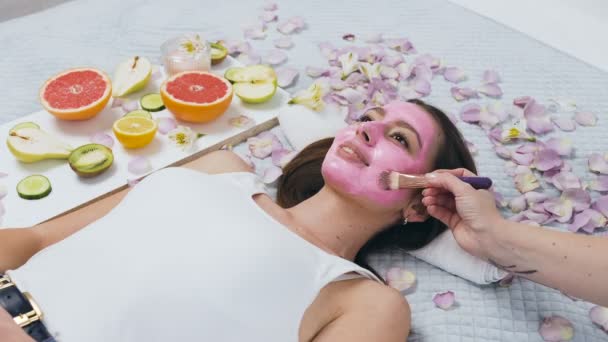 Pohled na atraktivní ženu relaxační ve wellness centru, zatímco beauticijník používá růžovou masku pomocí make štětců. — Stock video