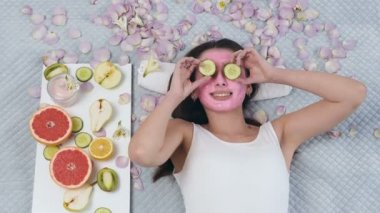 Yakışıklı kadının yüzünde pembe maske ile yatan ve sağlıklı yaşam merkezinde gözleri salatalık koyarak üst görünümü.