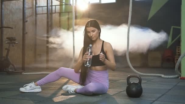 Красивая стройная женщина пьет воду во время отдыха после тренировки в тренажерном зале . — стоковое видео