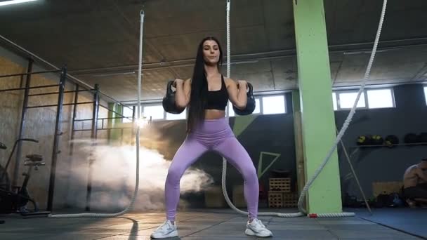 Vista inferior de la mujer de fitness enfocada haciendo sentadilla con peso en las manos en el gimnasio . — Vídeo de stock