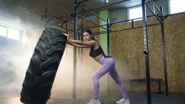 Silna młoda kobieta trzyma duże opony ciągnika i patrząc do aparatu podczas treningu Cross trening w siłowni. — Wideo stockowe