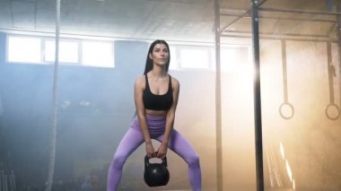 Crossfit spor salonunda elinde kettlebells ile çömelme Çekici uygun kadın.