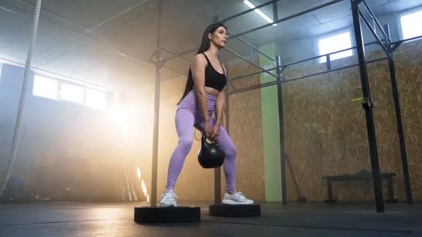 Confident sport woman squatting with kettlebells in the hands in crossfit gym. — Stock Video