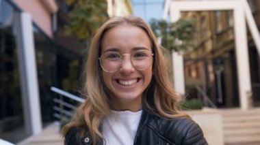 Sokak arka planda kamera karşısında gülümseyen gözlükuzun saçlı sevimli beyaz kadın yakın portresi. Açık havada