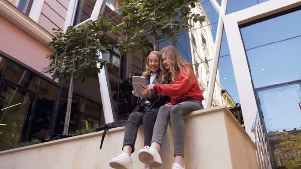 タブレットコンピュータを使用して良いニュースを読んでかなり若い女子学生は、屋外の大学で楽しみで昼休みを過ごす — ストック動画