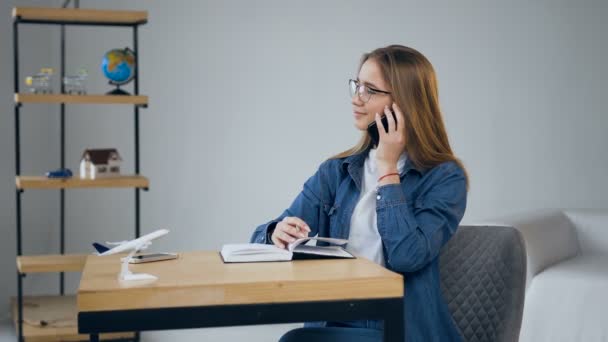 Knappe jonge vrouw die op de smartphone in het reisbureau praat. — Stockvideo