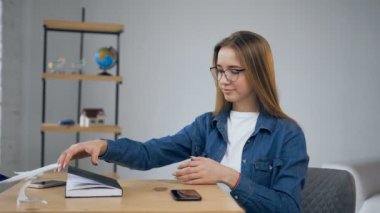 Sevimli genç kadın masaya akıllı telefon koyarak ve evde not defterine yazmaya başlayın.