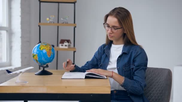 Fokussierte junge Frau schreibt Plan für zukünftige Reise ins Notizbuch. — Stockvideo
