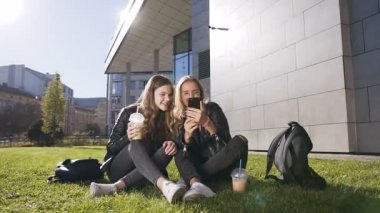 Akıllı telefon ile çekici genç kız güneşli havalarda parkta açık havada oturan internet üzerinden eğlenceli resimler gülüyor. Açık havada