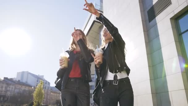 Две кавказские молодые подруги пьют свежий сок во время прогулки по городу возле современного здания в солнечный день. На открытом воздухе, образ жизни — стоковое видео