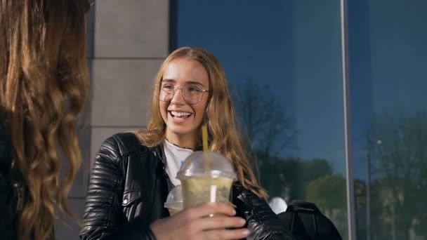 Две счастливые красивые девушки пьют молочные коктейли на открытом воздухе в летний солнечный день. Человек и дружба — стоковое видео
