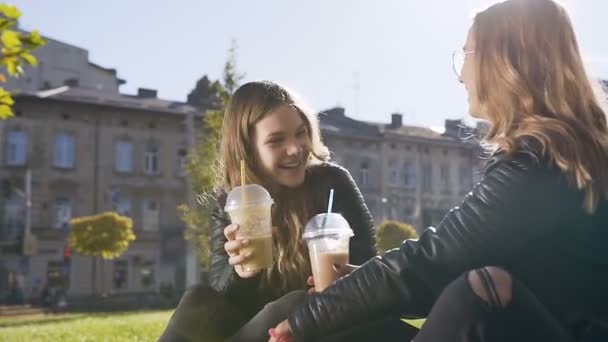 Mutlu kafkas üniversiteli kızlar süt kokteylleri ve ilginç konuşan bir şey içerken mola sırasında çim üzerinde oturan. İnsanlar, yaşam tarzı ve arkadaş kavramı — Stok video