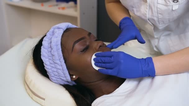 Primer plano de la cara de limpieza cosmetóloga femenina de la mujer africana joven usando almohadillas de algodón . — Vídeos de Stock