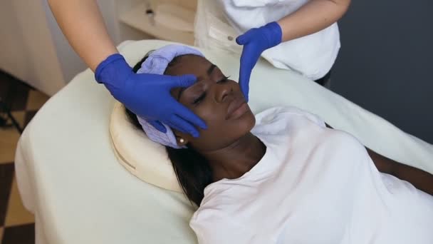 Cosmetoloog het maken van ontspannende massage aan de vrouwelijke Afrikaanse cliënt. — Stockvideo