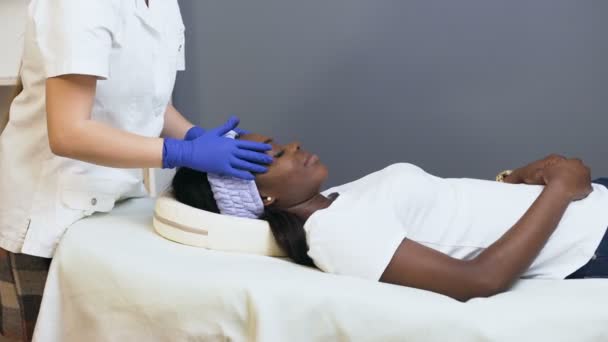 Ženská kosmetologa, která dělá uklidňující masáž africkému klientovi. — Stock video