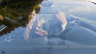 Cabriolet üzerinde yolculuk sırasında akıllı telefon kullanarak Çekici şık çift.