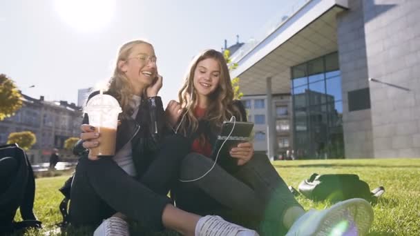 Gelukkige tiener vrienden met behulp van Tablet computer computer zittend op het gazon in Park in het centrum van de stad. Vriendschap, mens en technologie concept — Stockvideo