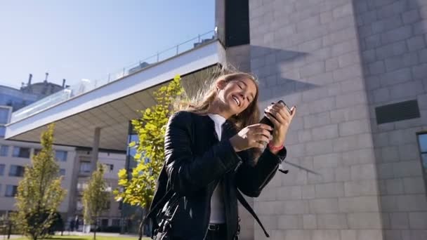 Портрет привлекательной молодой кавказки, использующей приложение на смартфоне и просматривающей текстовые сообщения во время прогулки по улице. Стиль жизни, городской — стоковое видео