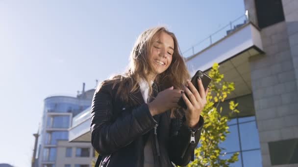 Bella studentessa che utilizza gadget digitale guardando i social media, leggendo notizie interessanti su app mentre cammina in città al tramonto. All'aperto, stile di vita — Video Stock
