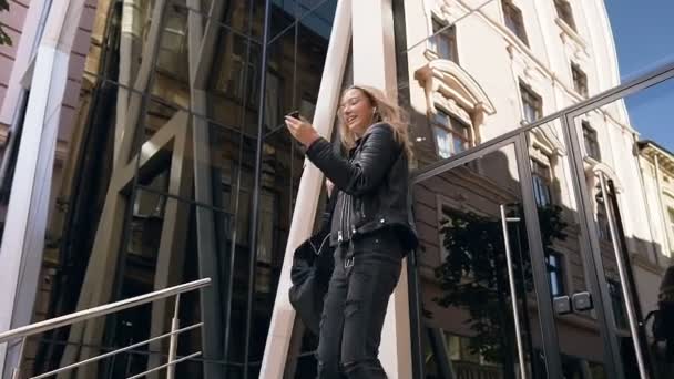 Alegre atractiva joven rubia bailando mientras baja las escaleras escuchando música en auriculares al aire libre cerca del moderno edificio de vidrio. Estilo de vida — Vídeos de Stock