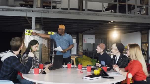 Afrikaanse mannelijke manager presenteert nieuwe business plan aan zijn cowoker tijdens zakelijke bijeenkomst in het kantoor. — Stockvideo