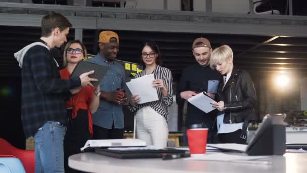 Team av unga hipster stående nära bord full av dokument, laptop, Tablet medan du arbetar tillsammans på den nya affärsplan. — Stockvideo