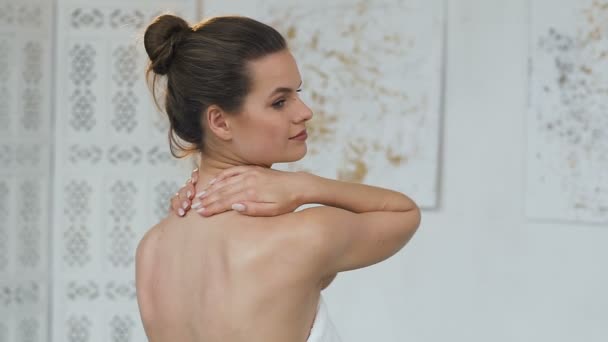 Schöne Frau massiert ihren Hals mit Creme auf dem weißen Badezimmerhintergrund. — Stockvideo