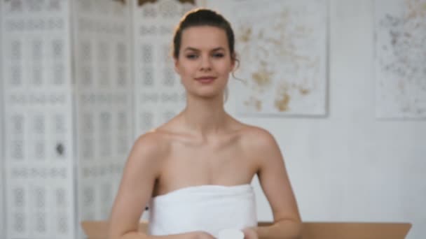 Hermosa mujer linda estirando el frasco con crema a la cámara en el fondo del baño . — Vídeo de stock