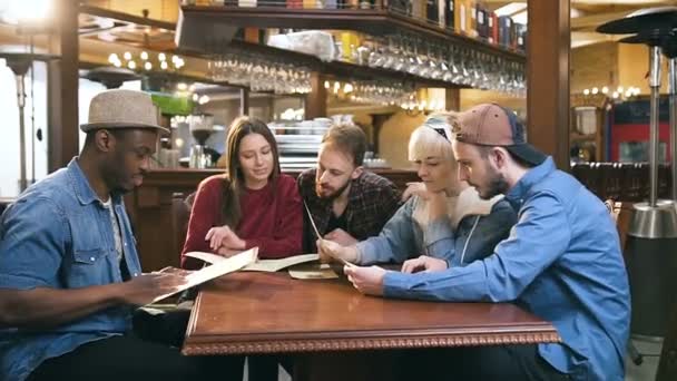 Companie de prieteni tineri care citesc meniul și aleg feluri de mâncare pentru ordine în bar, pub . — Videoclip de stoc