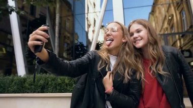 Komik yüzler yapan ve akıllı telefonda selfie fotoğrafı için gülümseyen genç kızlar. Açık havada. Dostluk, yaşam tarzı kavramı