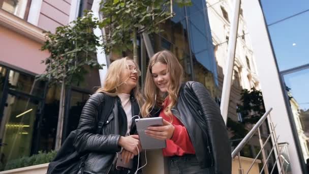 Schöne zwei Studentinnen, die mit Tablet-Computern gute Nachrichten lesen und die Mittagspause gerne im Freien verbringen. Freundschaft und Technologie-Konzept — Stockvideo