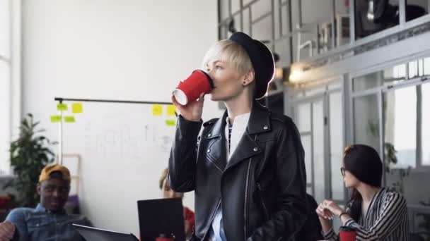 Creatieve Kaukasische zakenvrouw die koffie of thee drinkt terwijl haar team van multi-etnische zakenmensen belangrijke zaken op kantoor bespreekt — Stockvideo
