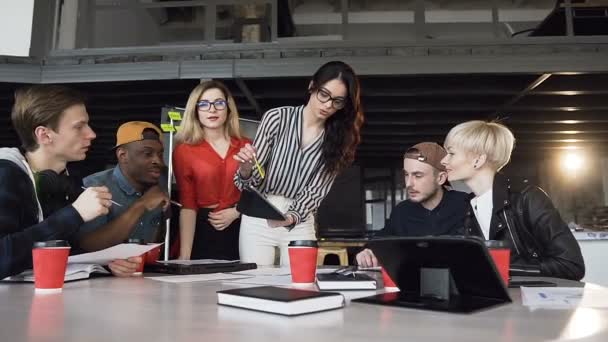 Líder da equipe feminina criativa em pé perto da mesa e dando direção à equipe criativa jovem em reunião no escritório. Brainstorming de jovens empresários — Vídeo de Stock