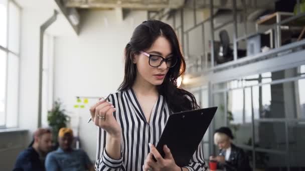 Retrato de una atractiva joven empresaria que trabaja con documentos en papel, haciendo algunas notas en cuaderno en la oficina. Tormenta de ideas, concepto de negocios y personas — Vídeos de Stock