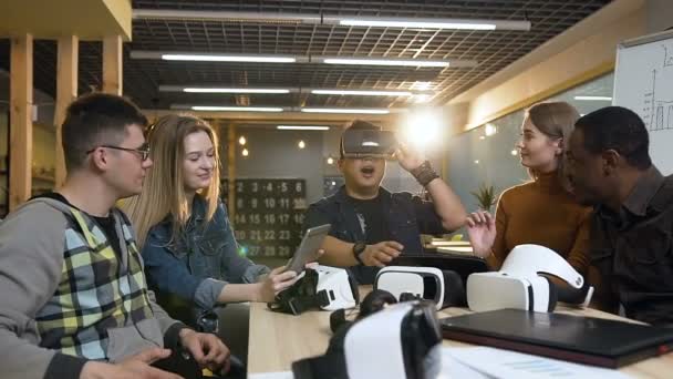 Joven hombre hipster en gafas de realidad virtual que se divierten jugando juego mientras sus vaqueros trabajan en la tableta, portátil . — Vídeos de Stock