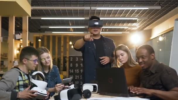 Grupa koncentruje ludzi pracujących na laptopie, tablet podczas gdy ich młody mężczyzna cowoker w wirtualnej rzeczywistości okulary zabawy gry. — Wideo stockowe