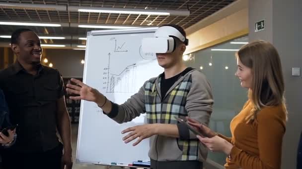 Pria muda Kaukasia mengenakan kacamata realitas maya bersenang-senang bermain game sementara para cowokers melihatnya . — Stok Video